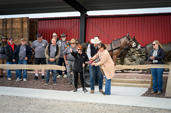 MB Garrison, Bo Tanner, and Claudia Tanner cut the ribbon in front of the restored 20 mule team while a group of people look on.